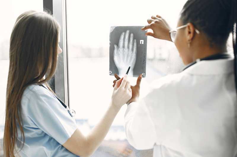 Two doctors by a bright window holding up and pointing at an X-ray of a hand