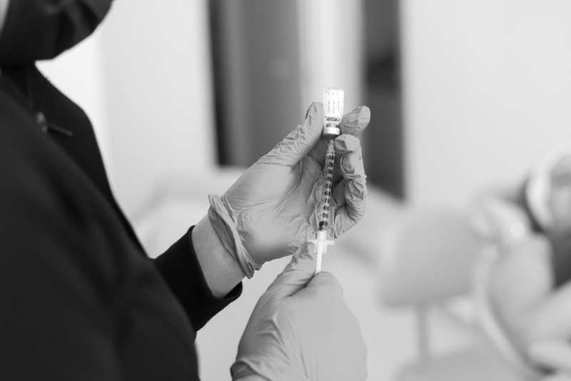 Black-and-white close-up of gloved hands drawing an injectable from a small vial into a syringe