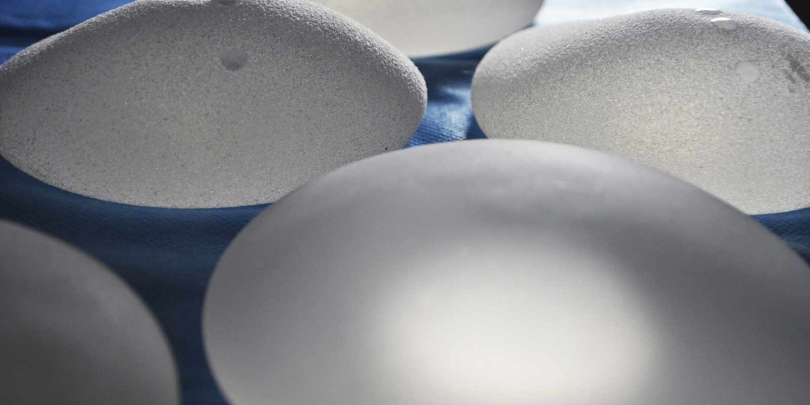 Several textured silicone breast implants lying on a blue sterile surgical drape